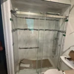 Shower stall with sliding glass doors and marble tiles, still under construction.