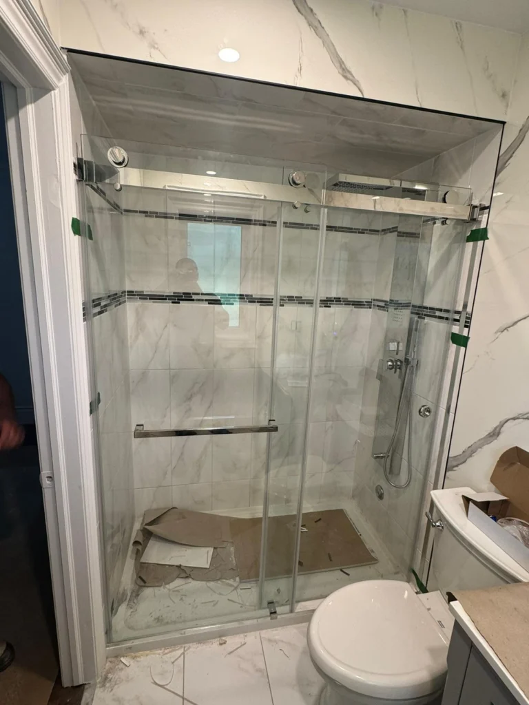 Shower stall with sliding glass doors and marble tiles, still under construction.
