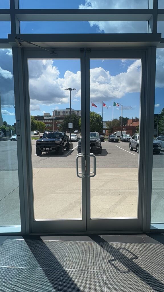 Glass doors with a view of cars parked outside, flags in the background, and clear sky