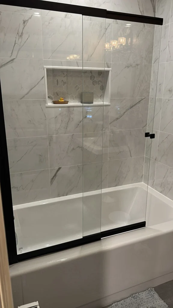 Modern shower with clear glass doors and white marble tiles.