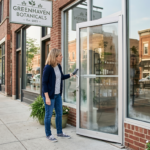 A small business owner is standing outside a storefront, inspecting the glass entrance and aluminum frame
